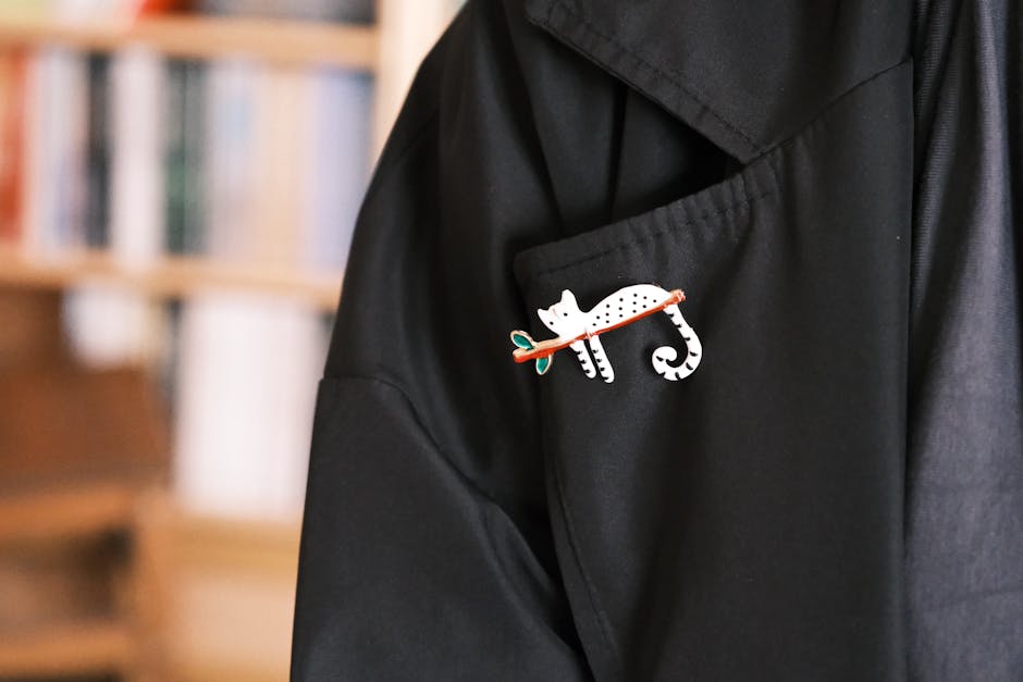 Stylish cat brooch on the pocket of a black jacket with books blurred in the background.
